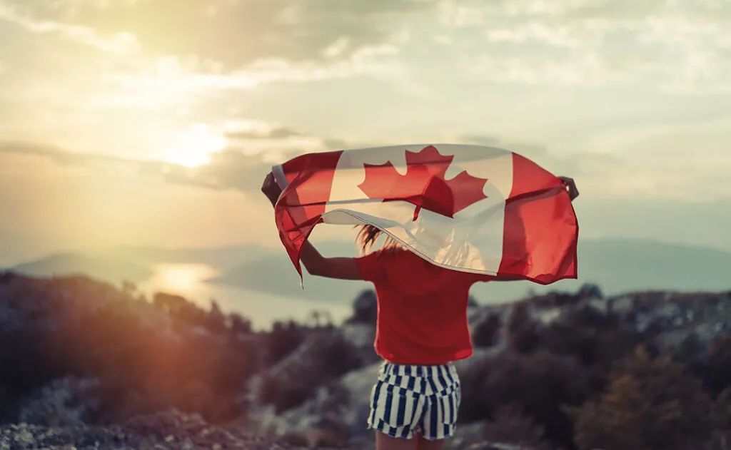 Happy child teenage girl waving the flag of Canada while running at sunset