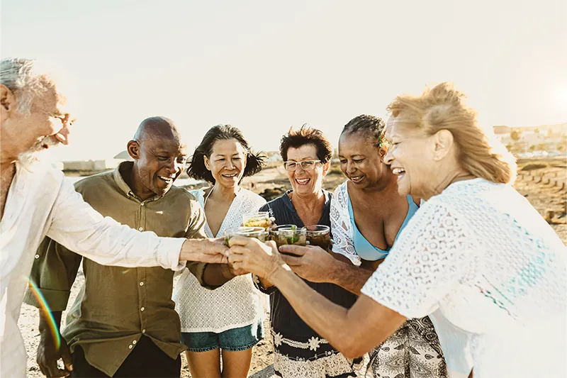 Group of senior friends toasting drinks on the beach