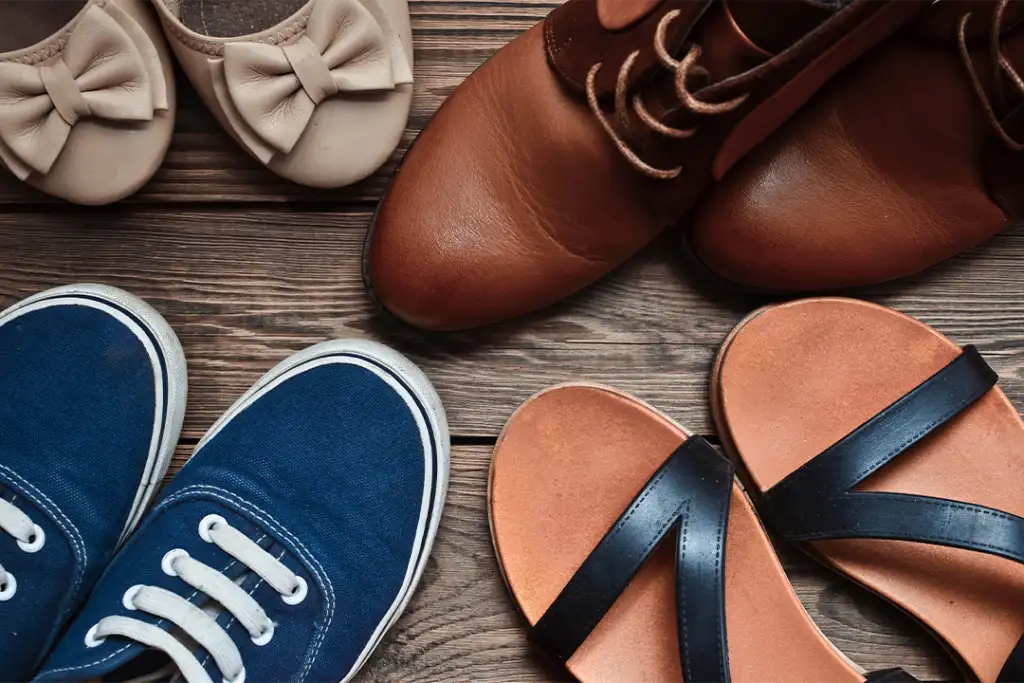 Women's shoes of different seasons on the wooden floor. Top view of sandals, boots, sneakers, ballet shoes.