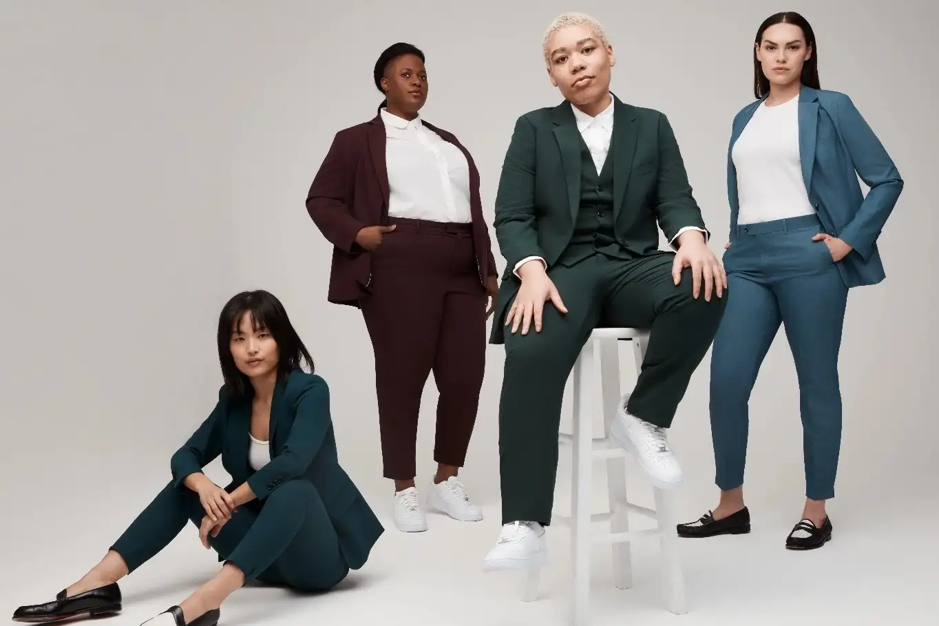 Four people of varying clothing sizes wearing suits from the Suit Shop, posing on a grey backdrop