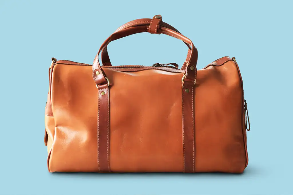 Large classic brown leather travel bag with light blue background